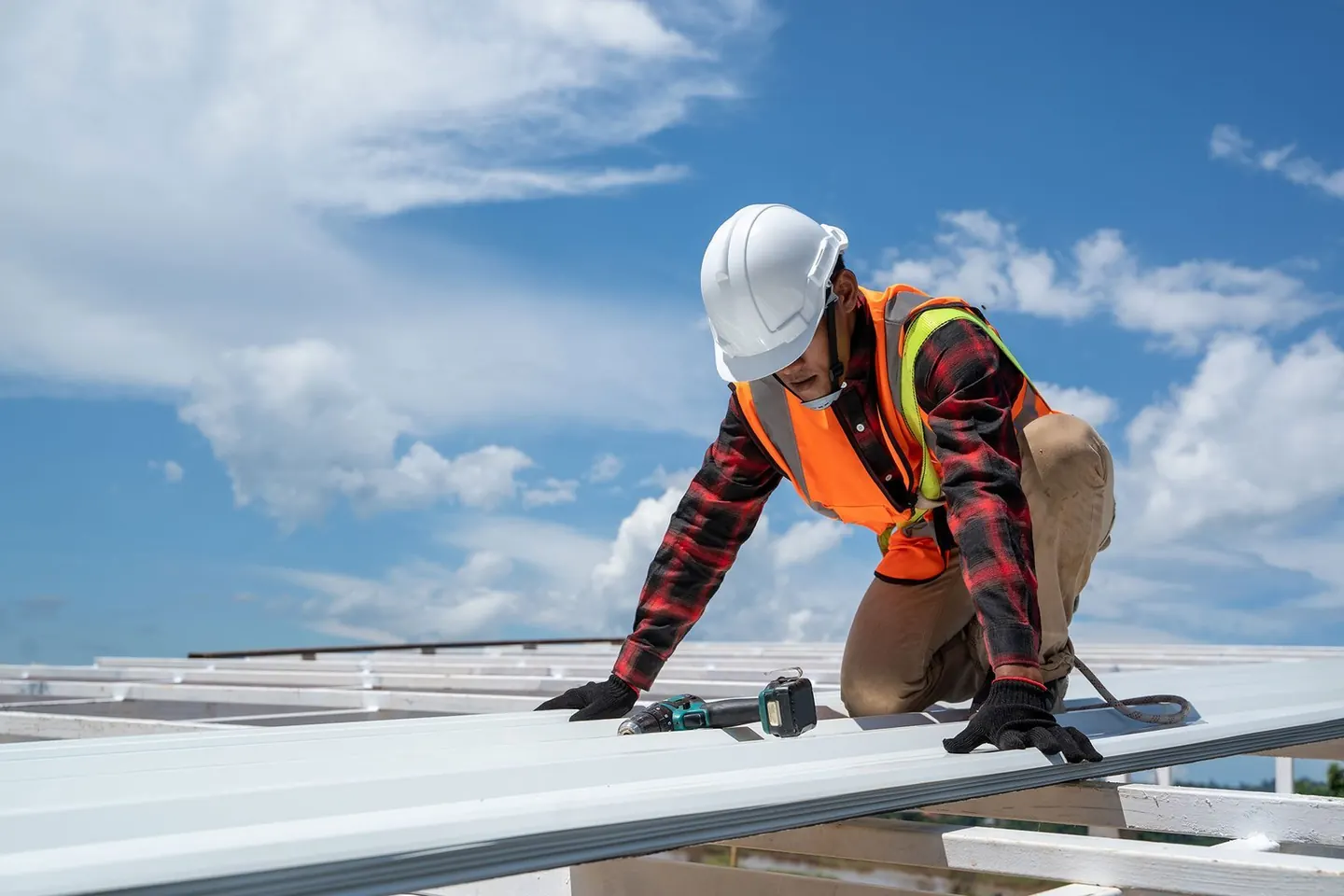 Roofer in work gloves screwing down steel roof sheeting